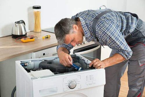 Un tuttofare esperto esamina attentamente l'interno di una lavatrice utilizzando una torcia elettrica, dimostrando competenza e precisione.