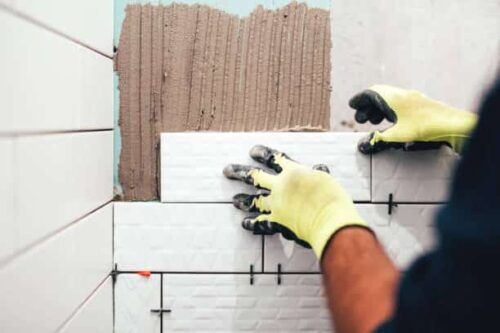 Esperto artigiano nel settore dell'edilizia posa accuratamente piastrelle di ceramica sulle pareti di un bagno, in un'attenta opera di dettaglio.