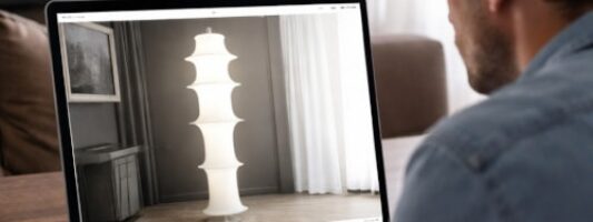 Cliente osserva online una lampada Made in Italy contraffatta su un sito di arredi di design, simbolo dei falsi arredi di lusso Made in Cina.