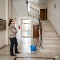 Condomina al piano terra davanti alle scale condominiali pulite con secchio e mocio.
