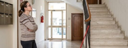Condomina al piano terra davanti alle scale condominiali pulite con secchio e mocio.