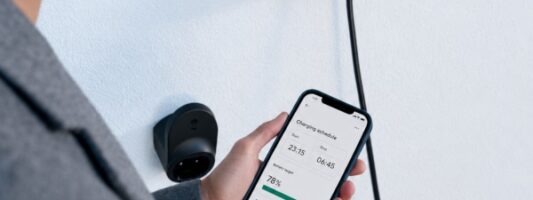 Persona che controlla una wallbox domestica per auto elettrica tramite smartphone.