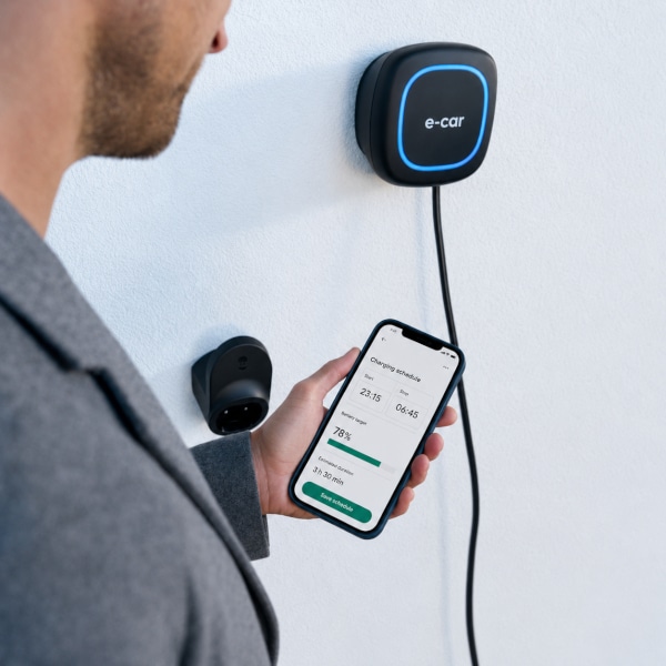Persona che controlla una wallbox domestica per auto elettrica tramite smartphone.