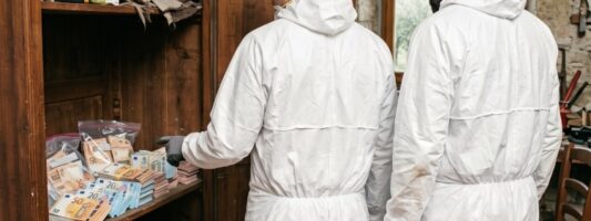 Due operatori in tute protettive bianche e guanti trovano mazzette di banconote di Euro nell'armadio di legno in casa da bonificare nelle campagne di Cingoli.