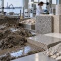 Fanghi di dragaggio e scarti della lavorazione della pietra accanto a piastrelle finite, simbolo del recupero dei materiali in edilizia.
